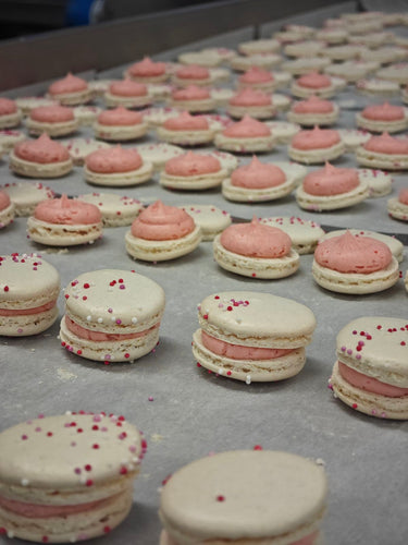 Champagne & raspberry macarons laid out on a kitchen bench.