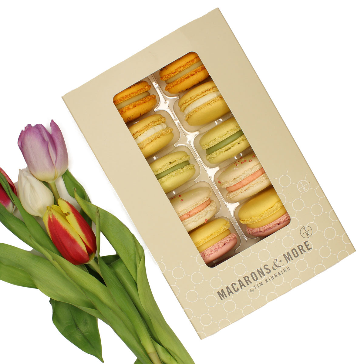 Box of colourful macarons next to a bouquet of tulips on a white background