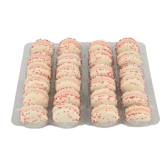 A tray of white Champagne & Raspberry macarons with red sprinkles on top, presented in clear packaging.