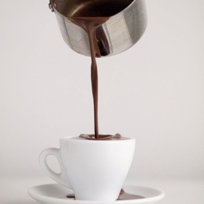 Melted chocolate being poured into a white espresso cup.