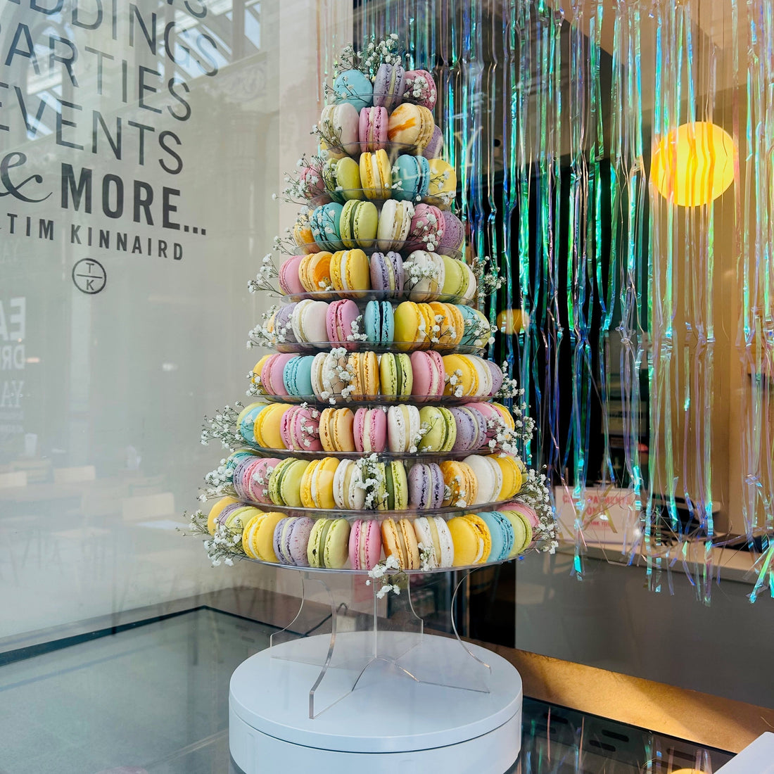 10 tier macaron tower for wedding receptions. Mixed coloured macarons, with flowers added on display in a shop window.