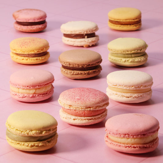 11 multicoloured macarons placed in rows on a pink surface