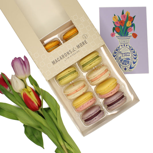 Box of macarons with a bouquet of tulips and a card showing a decorative vase on a white background.