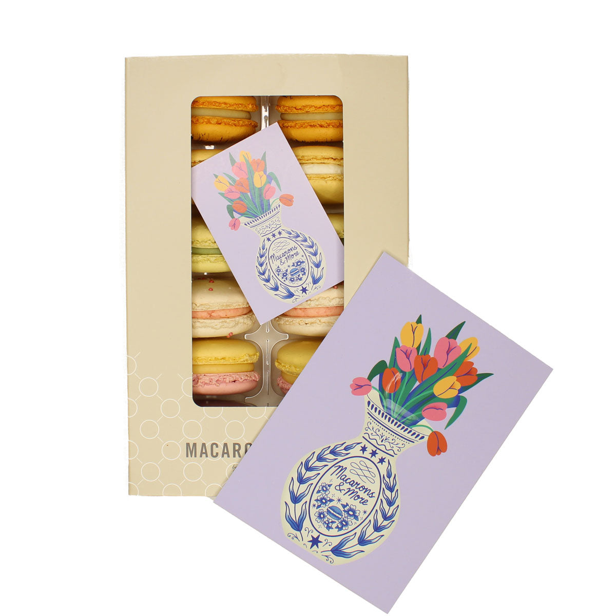 Box of macarons with a decorative vase with tulips in on a card, on a white background.