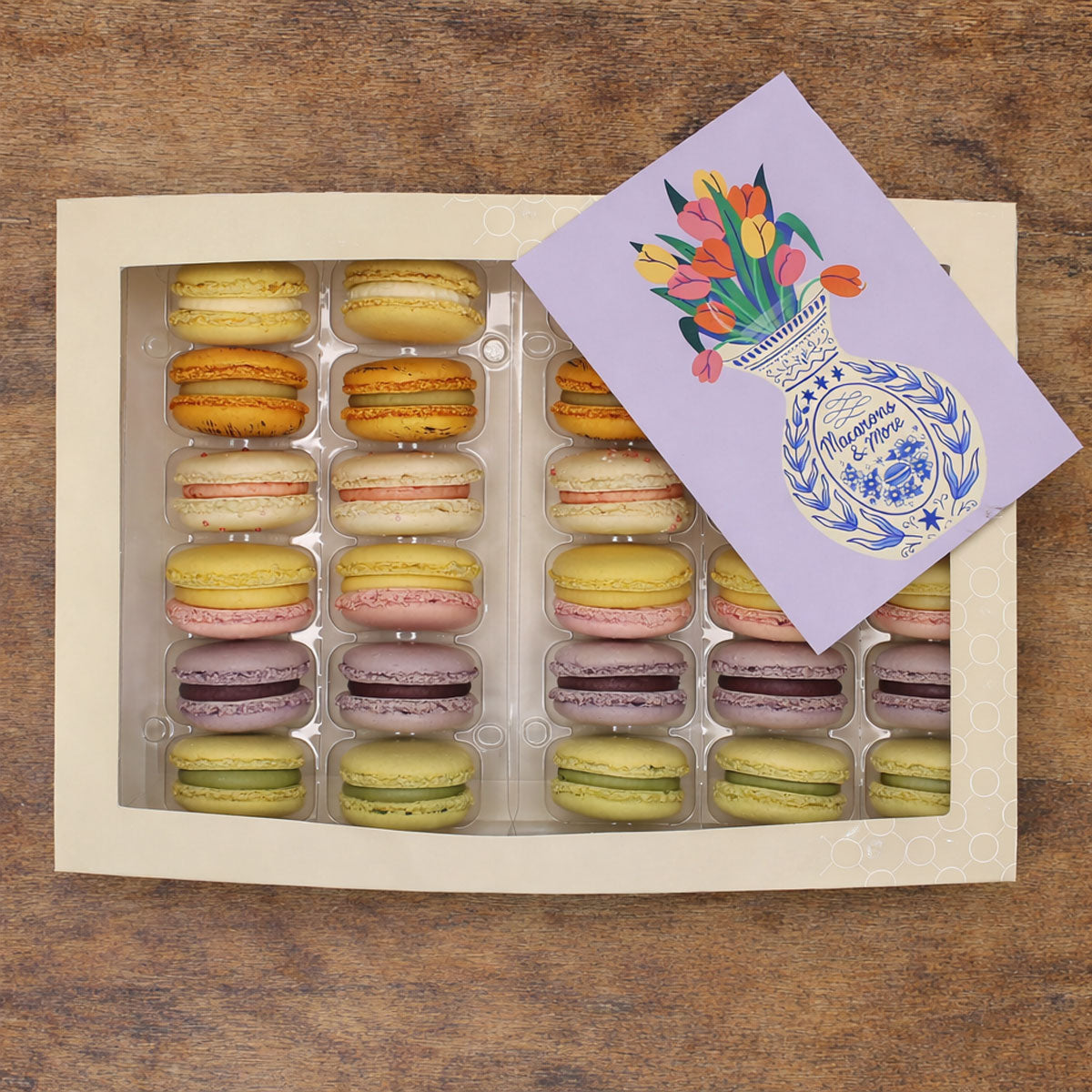 Box of colorful macarons with a decorative card on a wooden surface