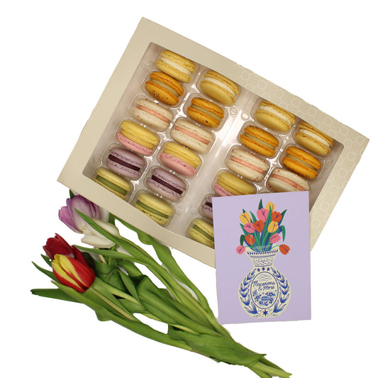 Box of macarons with a bouquet of tulips and a card on a white background