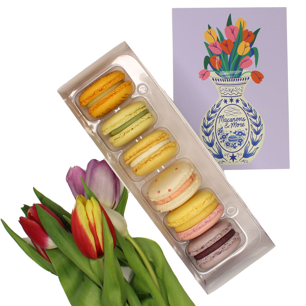 Box of colourful macarons next to a bouquet of tulips with a decorative card in the background.