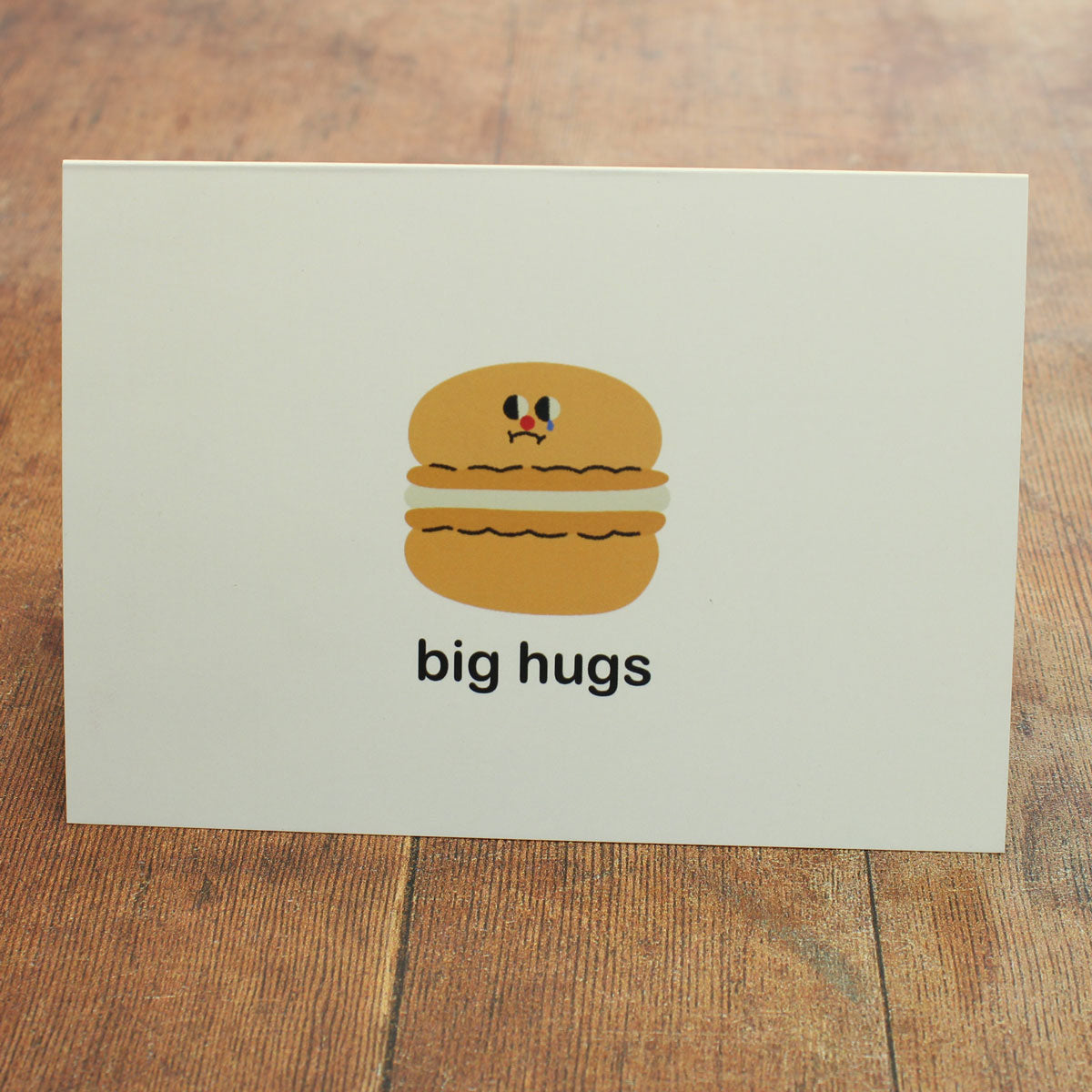 Card with a cartoon macaron and 'big hugs' text on a wooden surface