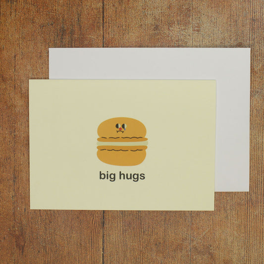 Card with a cartoon macaron and 'big hugs' text on a wooden surface
