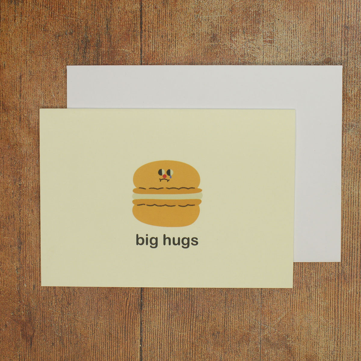 Card with a cartoon macaron and 'big hugs' text on a wooden surface