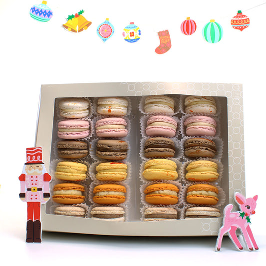Box of assorted Christmas macarons with Christmas-themed decorations on a white background