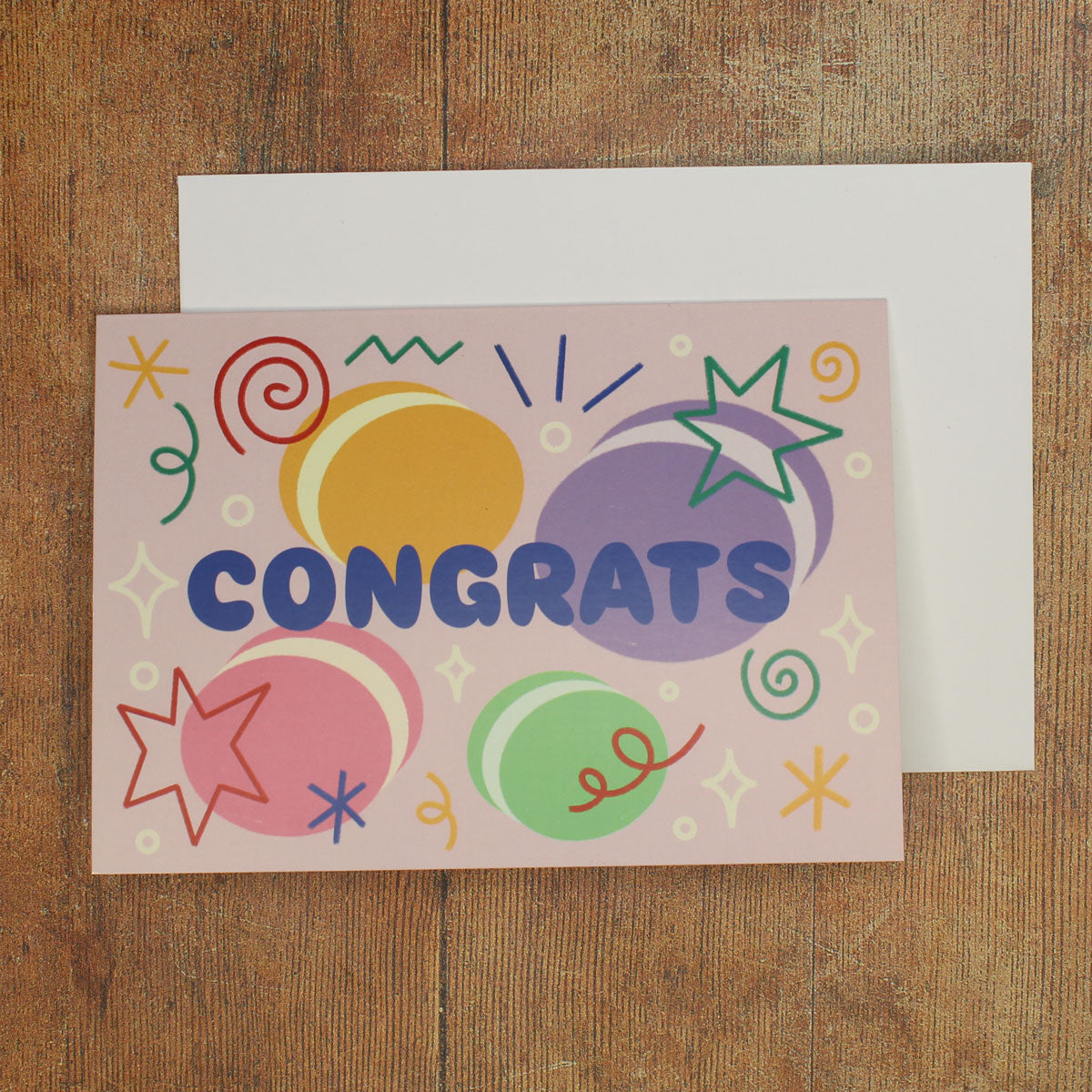 Colourful card with 'Congrats' text with macaron illustrations and stars and swirls on a wooden surface