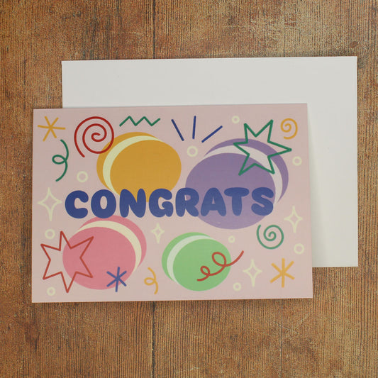 Colourful card with 'Congrats' text with macaron illustrations and stars and swirls on a wooden surface