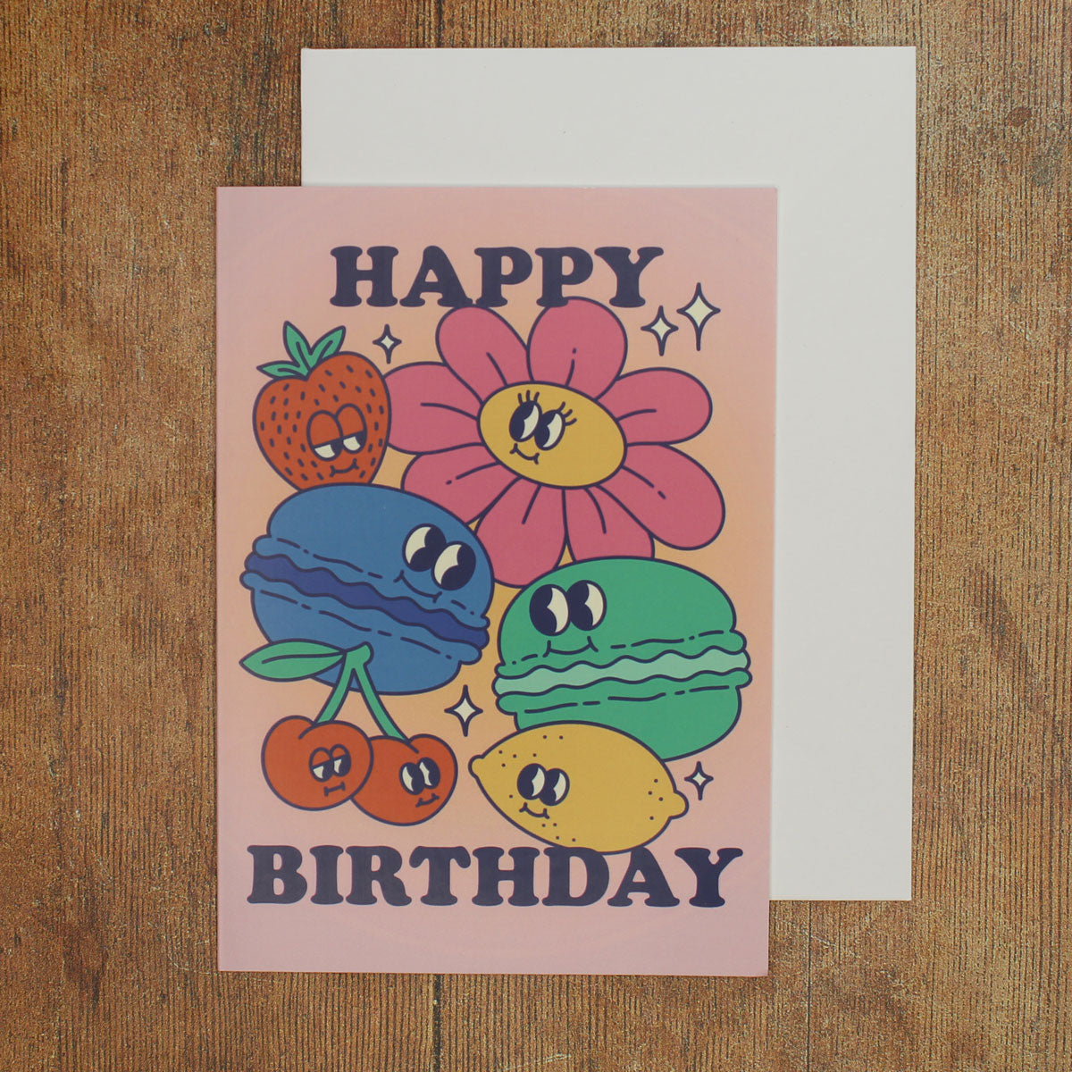 Pink card with colour illustrations of cartoon macarons, fruits and flowers with the text 'happy birthday'