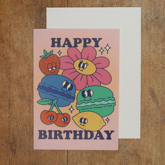 Pink card with colour illustrations of cartoon macarons, fruits and flowers with the text 'happy birthday'
