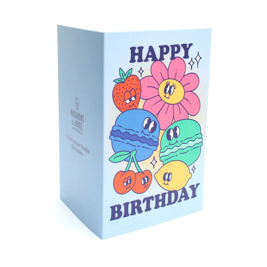 Blue card with colour illustrations of cartoon macarons, fruits and flowers with the text 'happy birthday'