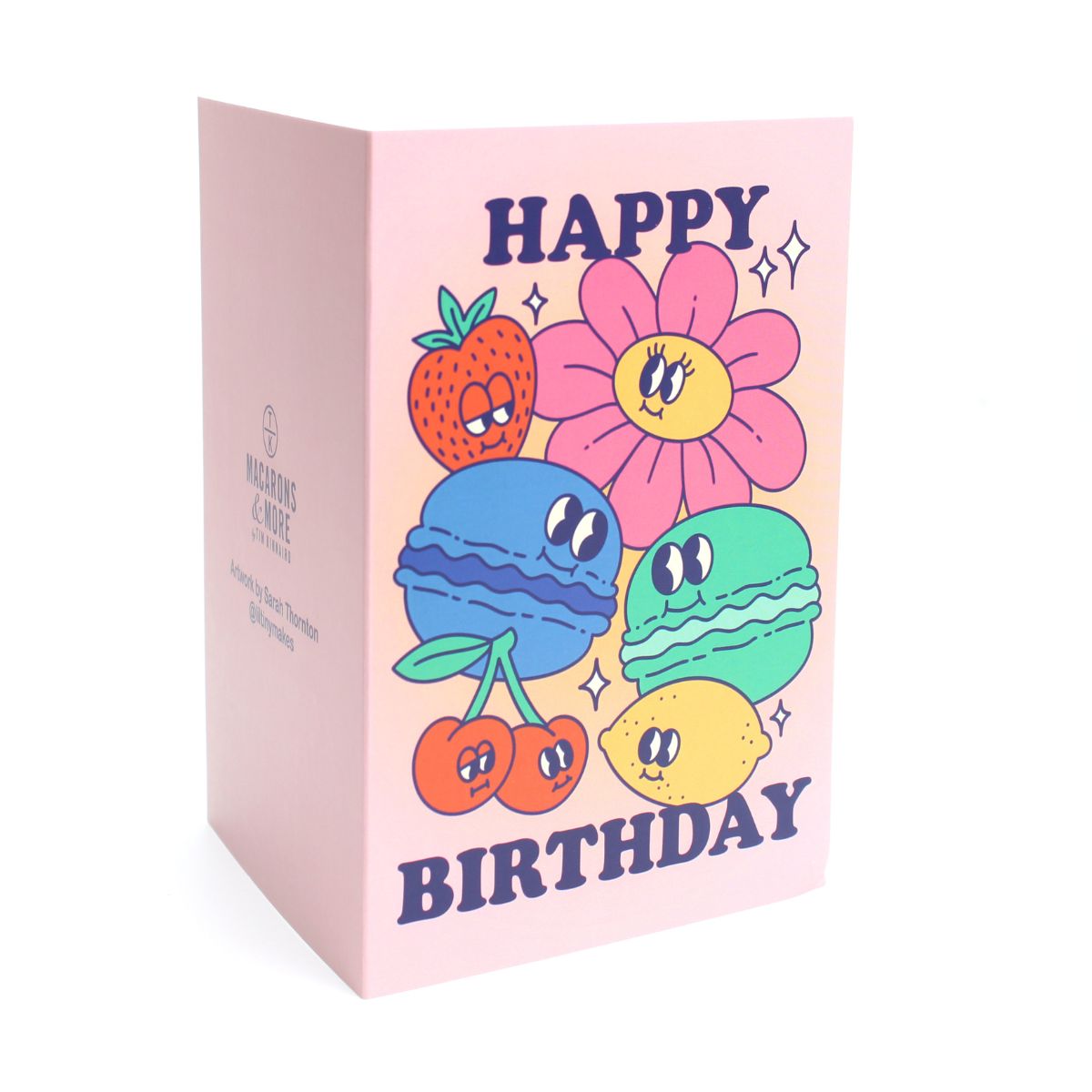 Pink card with colour illustrations of cartoon macarons, fruits and flowers with the text 'happy birthday'
