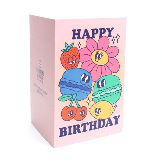 Pink card with colour illustrations of cartoon macarons, fruits and flowers with the text 'happy birthday'