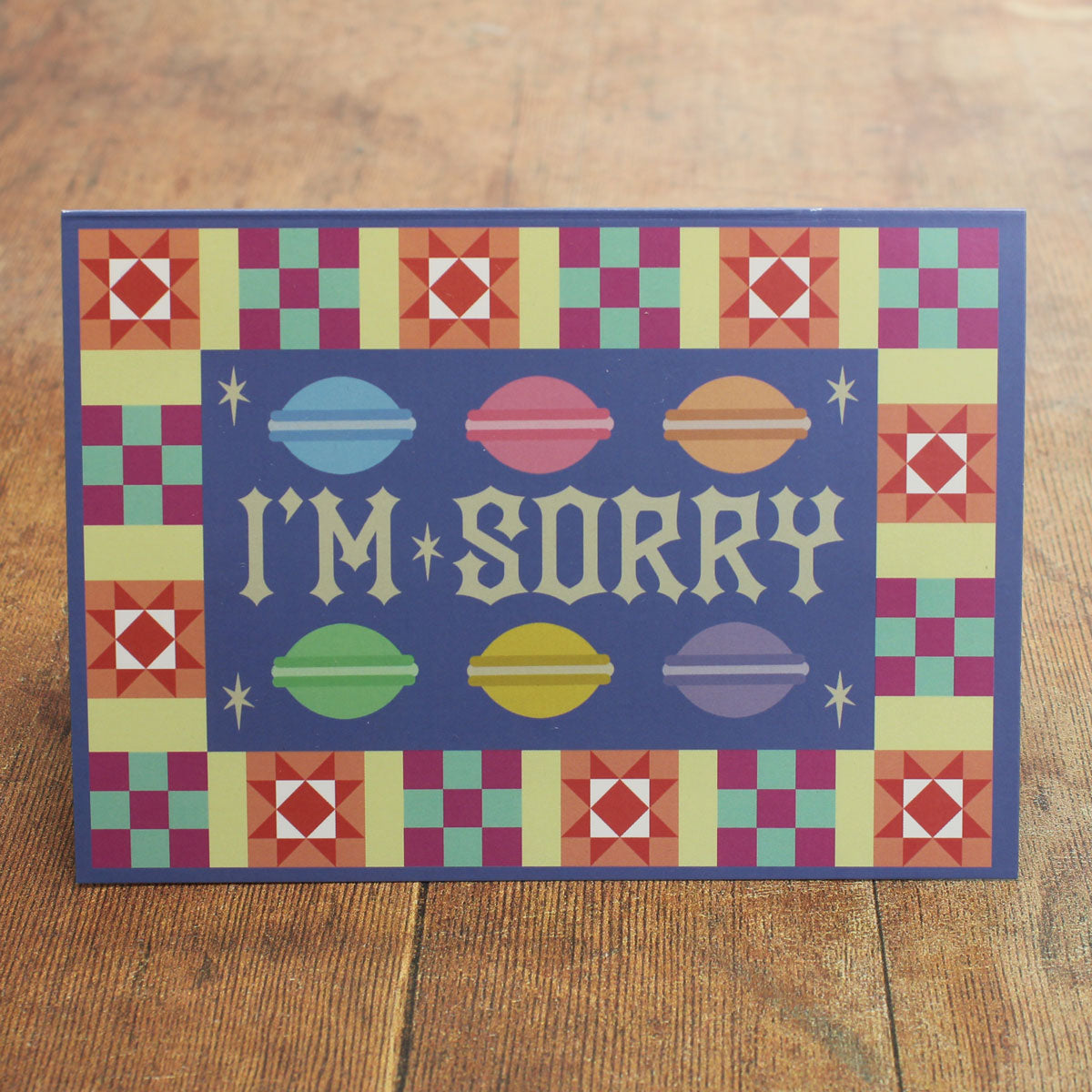 Blue card with colour macaron illustrations  and a colourful border with 'I'm Sorry' text  on a wooden surface