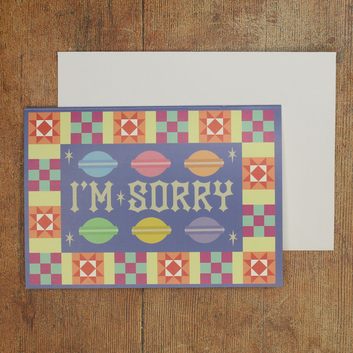 Blue card with colour macaron illustrations  and a colourful border with 'I'm Sorry' text  on a wooden surface