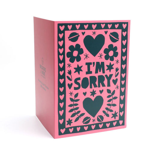 Card with 'I'm Sorry' text on a pink background with black hearts and flowers and macarons 