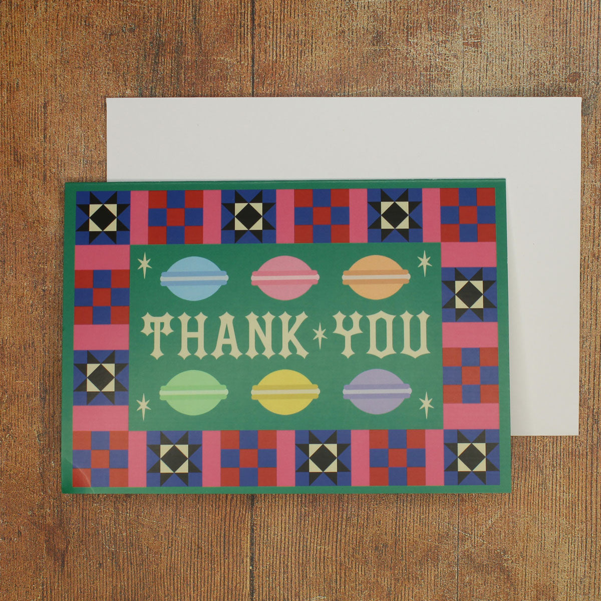 Green card with colourful  macaron illustrations and a colourful border with 'Thank You' text  on a wooden surface