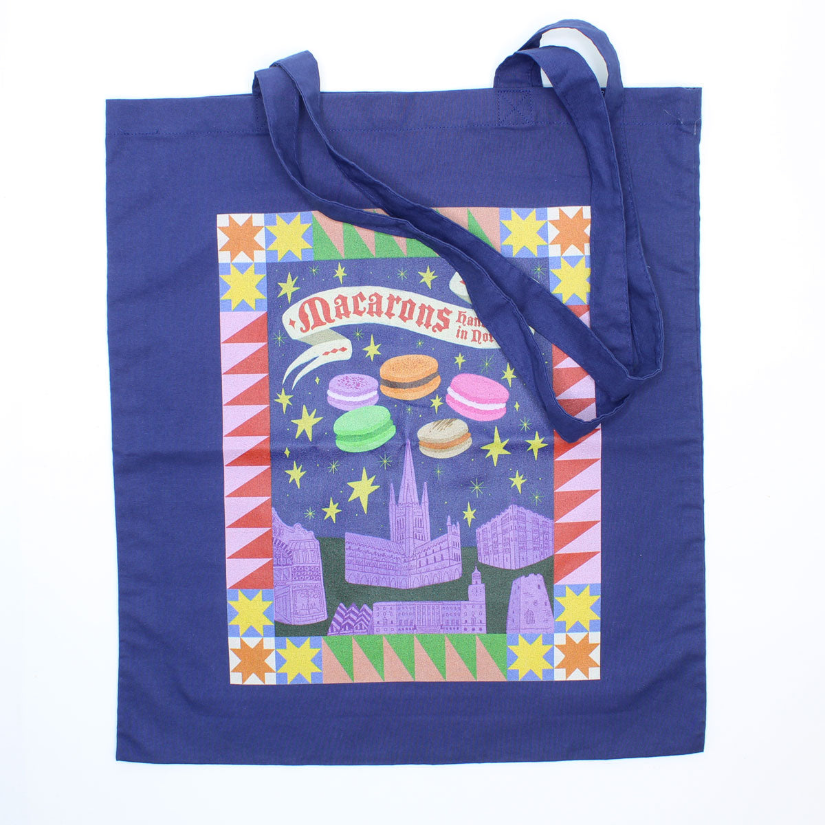 Blue tote bag with colourful design featuring macarons and Norwich castle and Cathedral on a white background