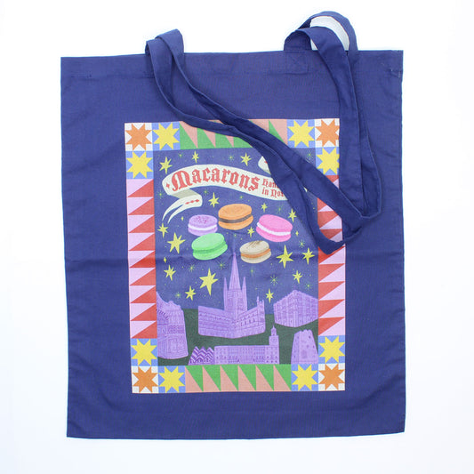 Blue tote bag with colourful design featuring macarons and Norwich castle and Cathedral on a white background