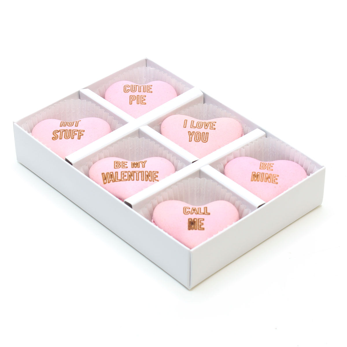 Box of pink heart-shaped valentine macarons engraved with 'love-heart' style messages on a white background