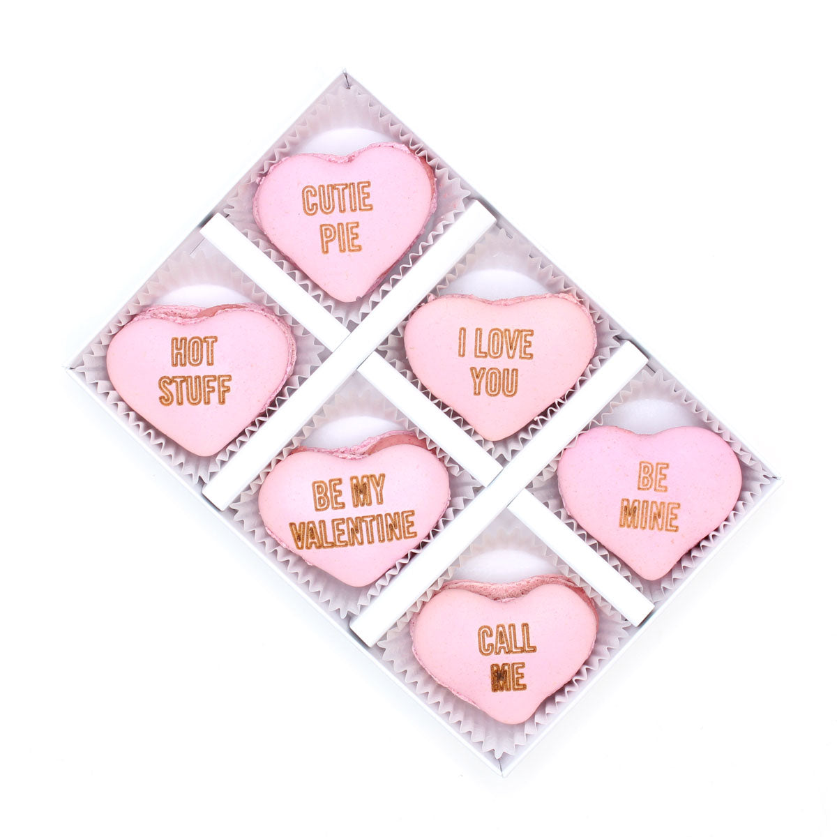 Pink heart-shaped macarons with various messages in a box on a white background