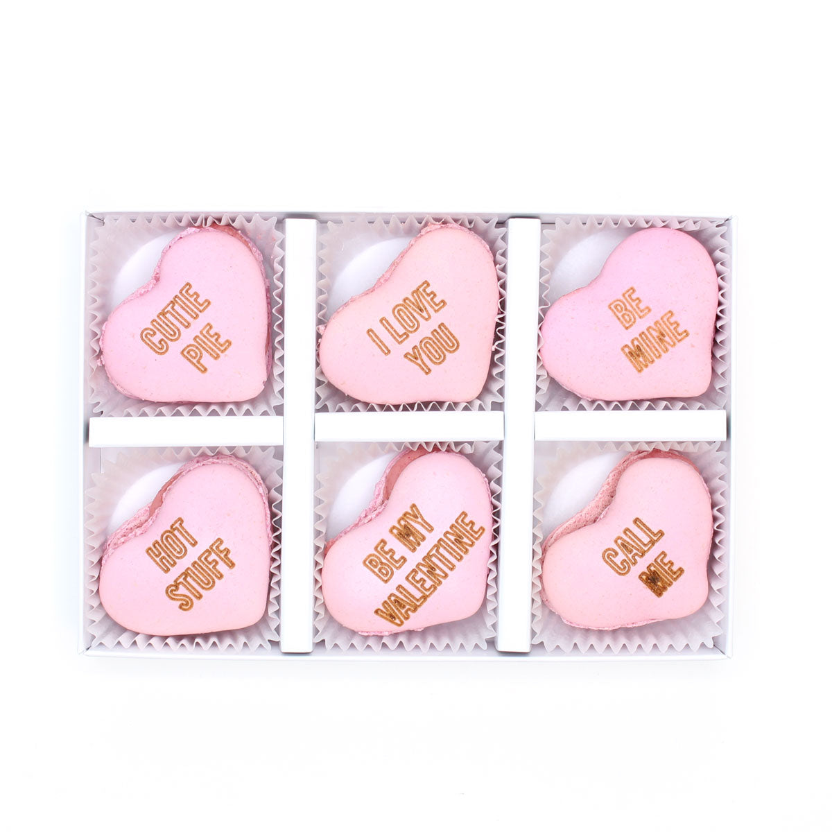 Set of pink heart-shaped macarons engraved with 'love-heart' style messages, in a white box on a white background.