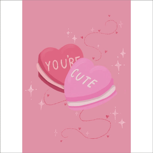 Soft pink A6 card featuring two heart shaped macarons with the words "YOU'RE CUTE" on.