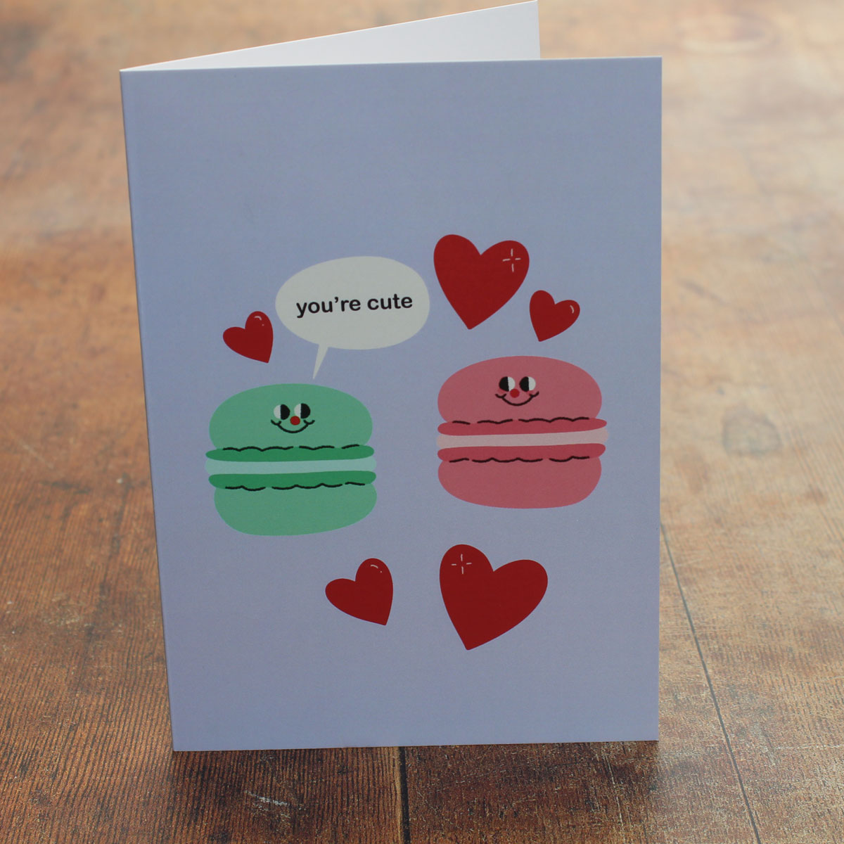 Card with cartoon macarons and hearts with a speech bubble reading 'you're cute'