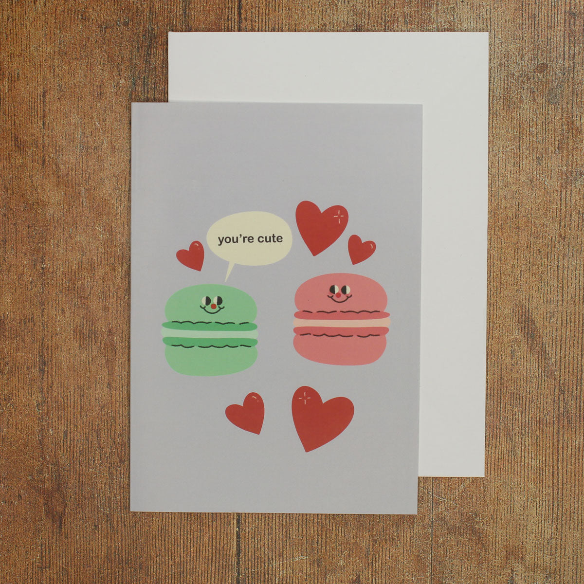 Card with cartoon macarons and hearts with a speech bubble reading 'you're cute'