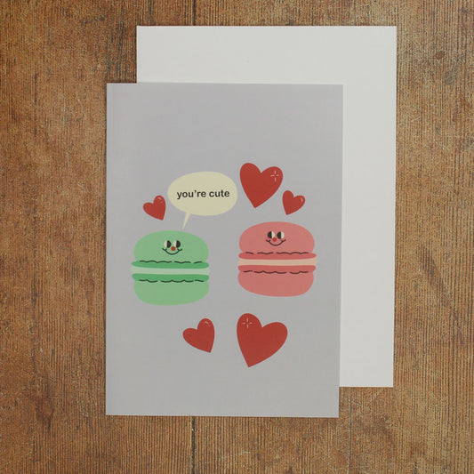 Card with cartoon macarons and hearts with a speech bubble reading 'you're cute'