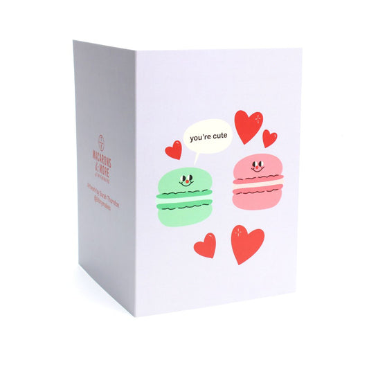 Card with cartoon macarons and hearts with a speech bubble reading 'you're cute'