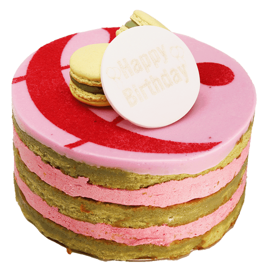 A Raspberry & Pistachio cake with multiple layers, toped with icing, macarons and a curly ampersand design and a 'Happy Birthday' plaque.